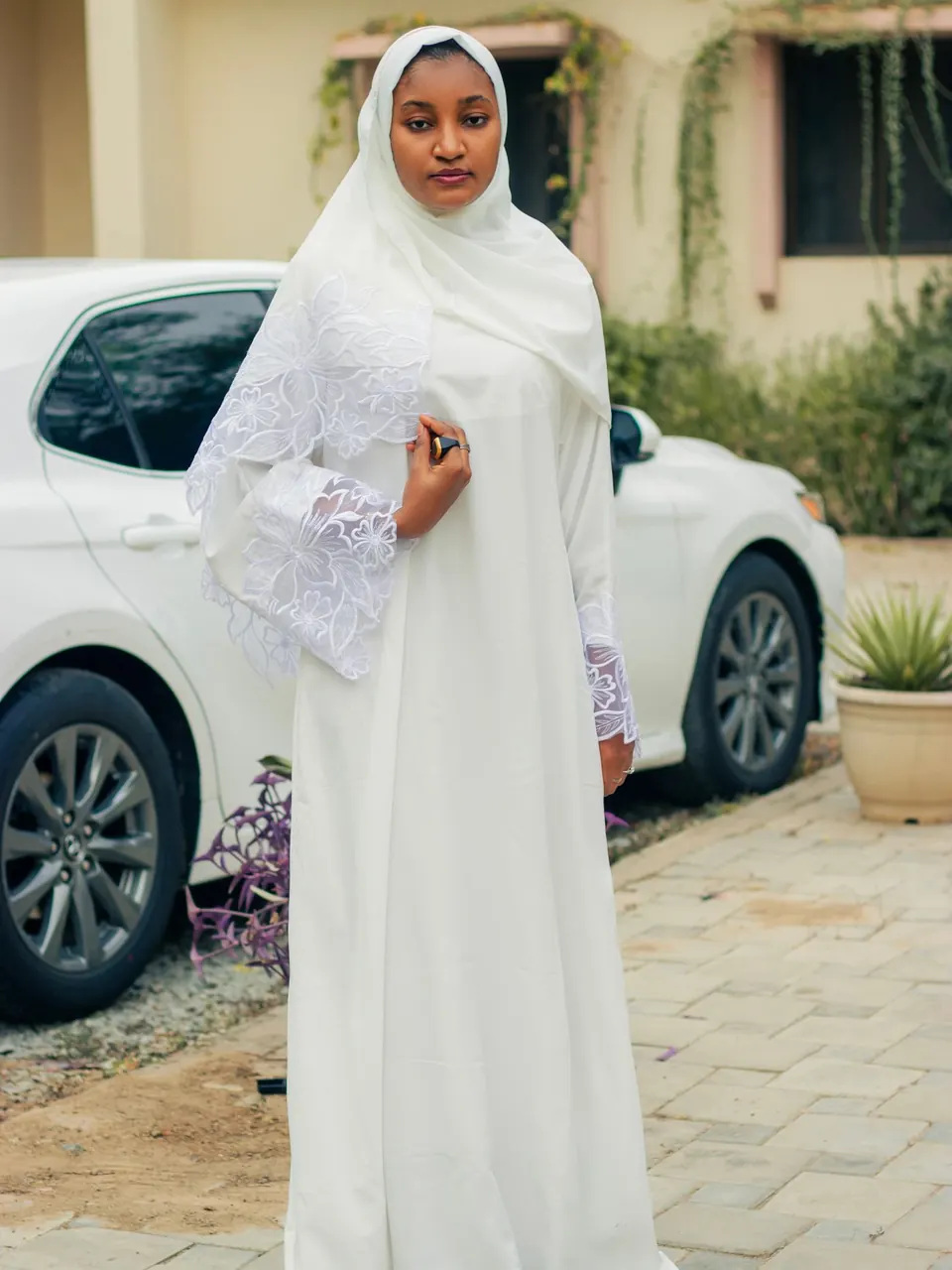 Une femme en abaya blanche et voile blanc, dans une allée ensoleillée