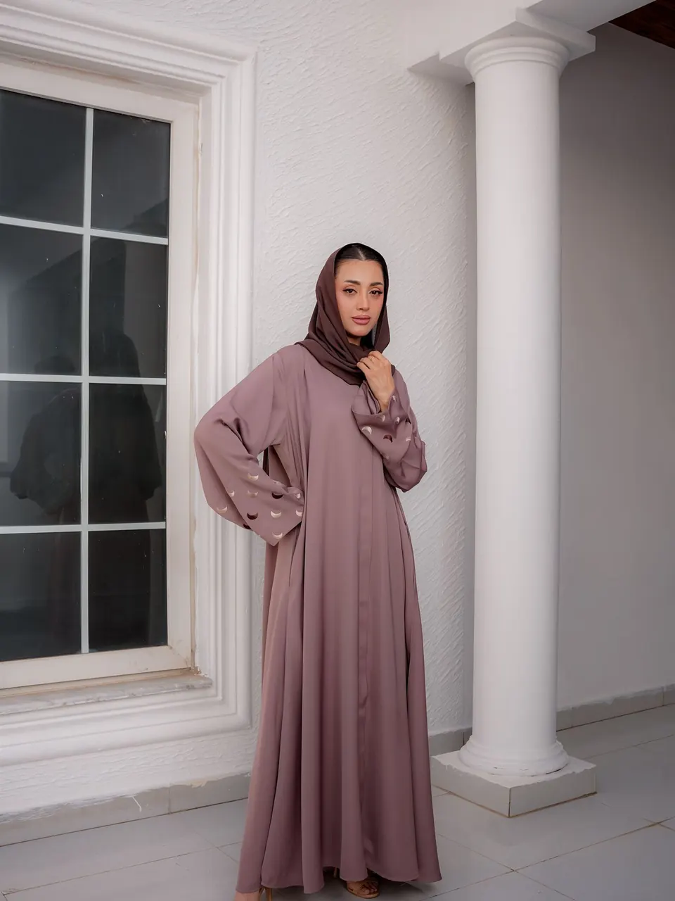 Une femme en abaya mauve et voile assorti, dans un salon clair