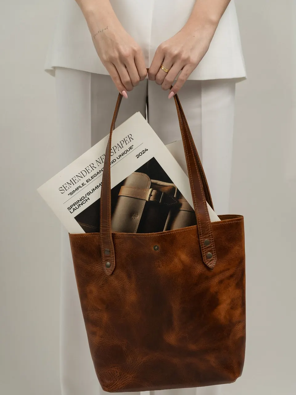 Un cabas en cuir cognac tenu à deux mains, un magazine dedans