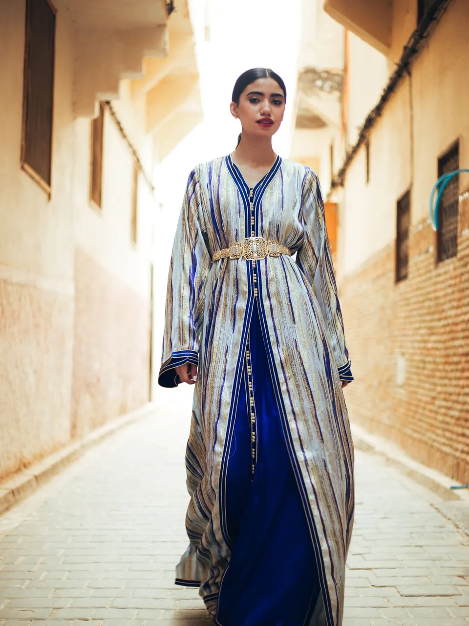 Une femme en caftan rayé marchant dans une ruelle de médina