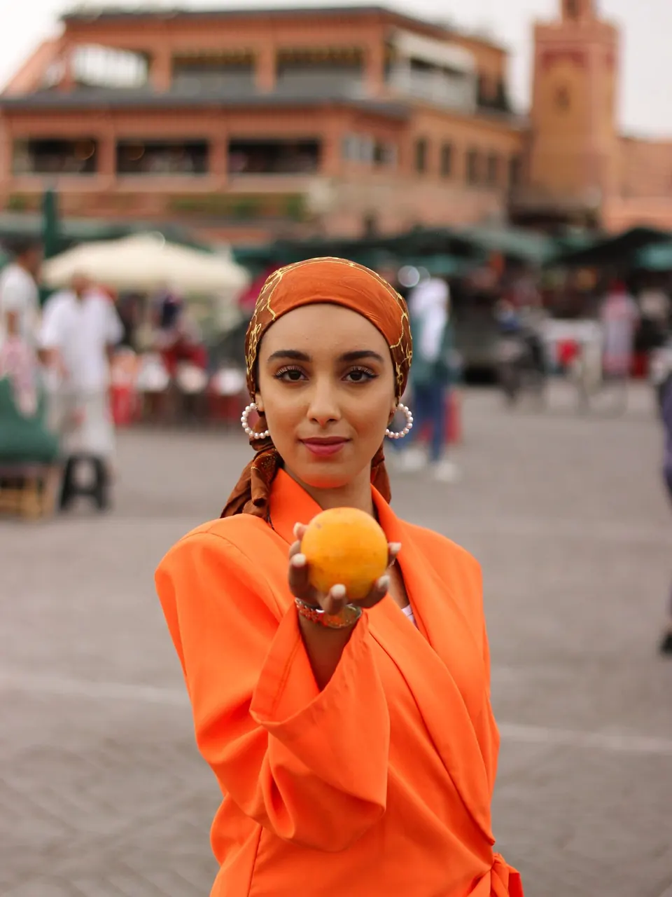 Une femme en tenue orange tenant une orange, place Jemaa el-Fna