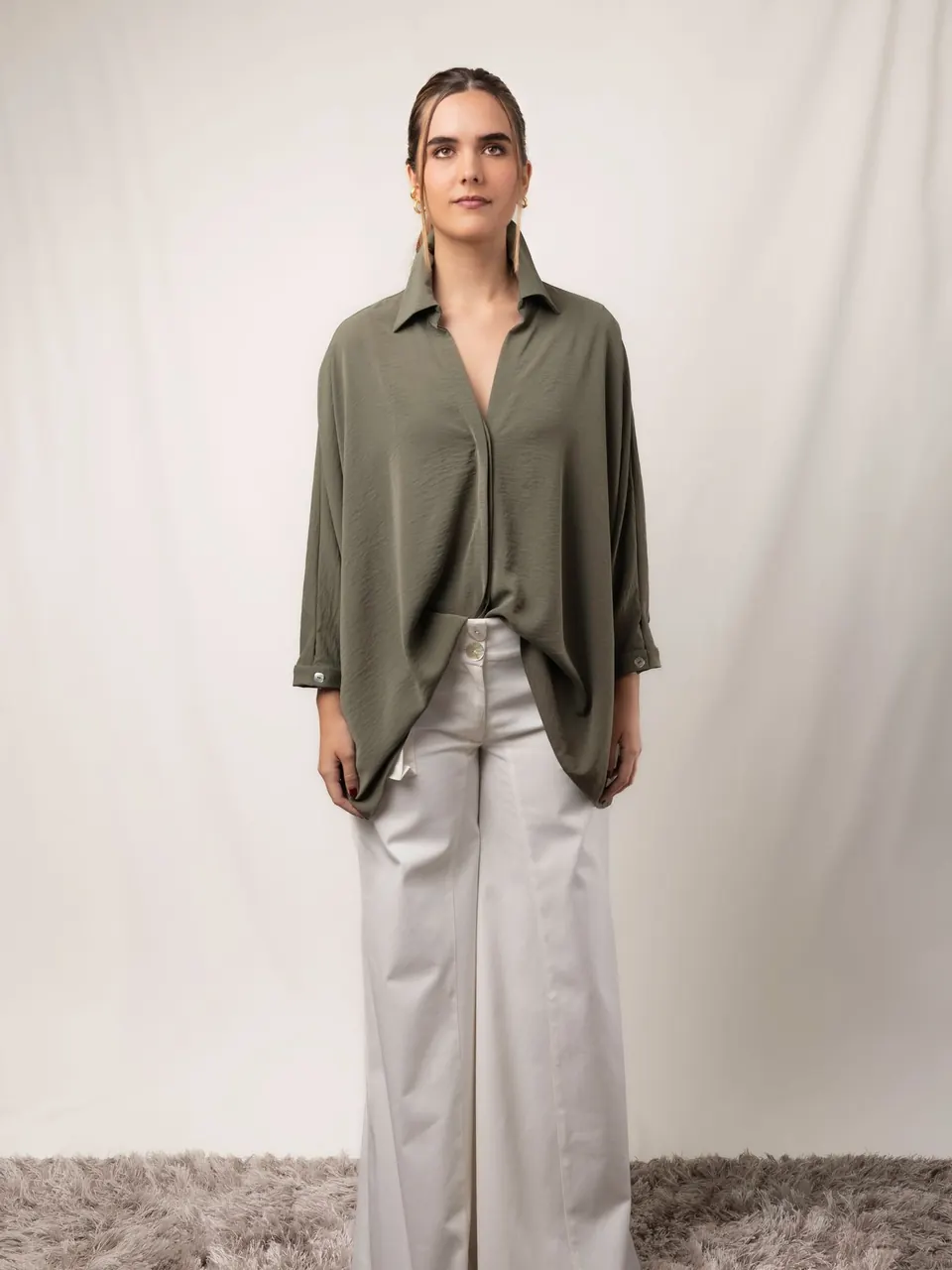 Une femme en chemise olive ample et pantalon large crème, en studio