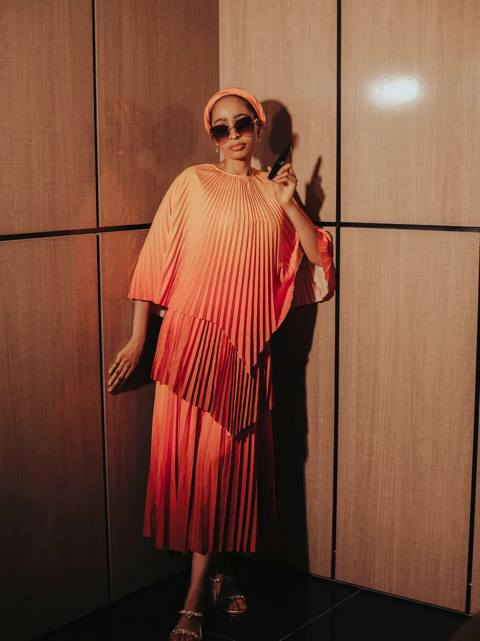 Une femme en robe plissée au dégradé corail et rouge