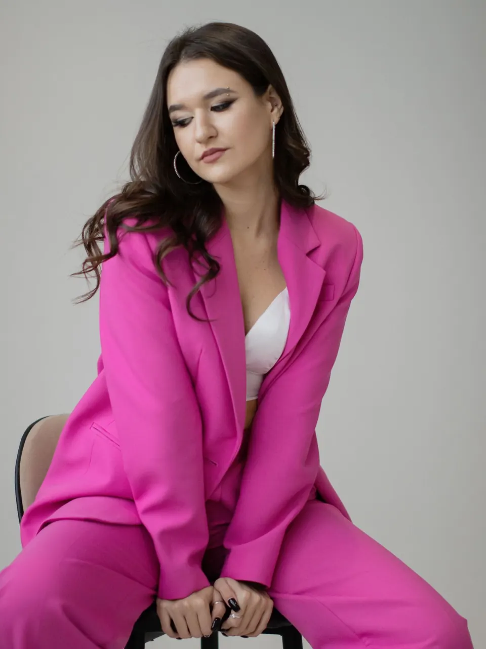 Une femme en tailleur fuchsia assise sur un tabouret, en studio