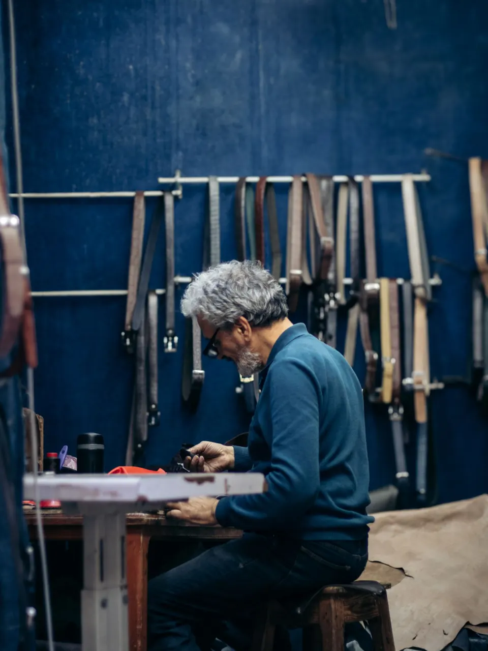 Un artisan travaille le cuir dans un atelier aux murs couverts de ceintures