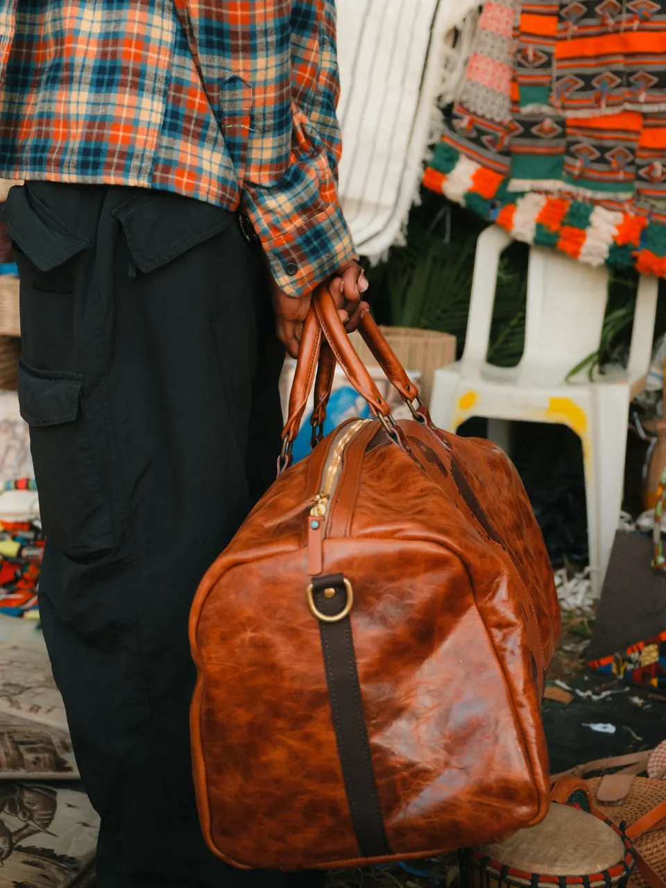 Une sacoche de voyage en cuir cognac portée à la main, dans un marché